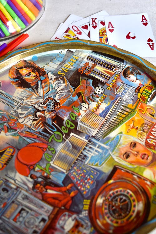 Top view of round metal tray representing colorful gambling and people near various cards with kit of stationery on table at home