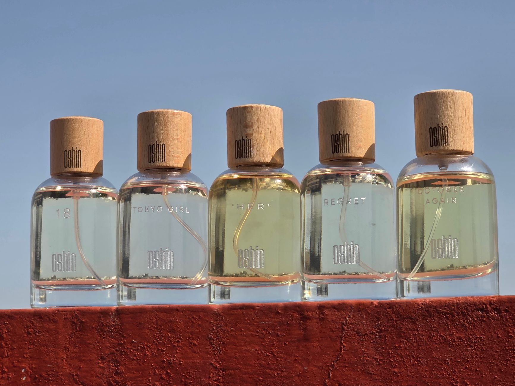 A collection of Oshin perfume bottles displayed outdoors with clear blue sky background.