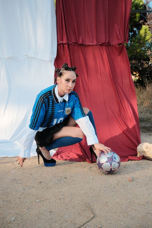 Free Fashionable woman posing in soccer jersey outdoors with a soccer ball, showcasing sports and style. Stock Photo