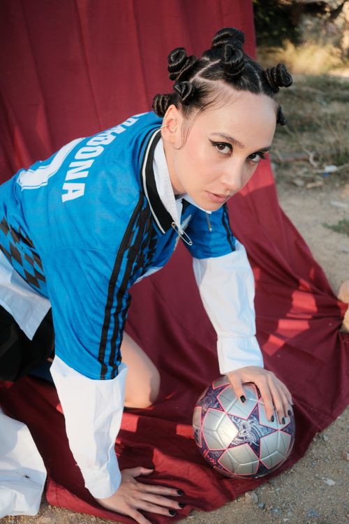 Free Confident female soccer player in stylish sportswear poses on a red backdrop with a soccer ball outdoors. Stock Photo