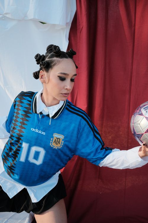 Free A woman poses artfully wearing an Argentine soccer jersey, holding a ball. Stock Photo