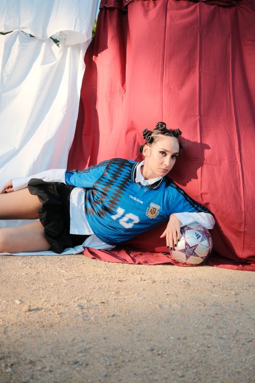 Free Youthful soccer fan in sports attire poses creatively with a soccer ball outdoors. Stock Photo