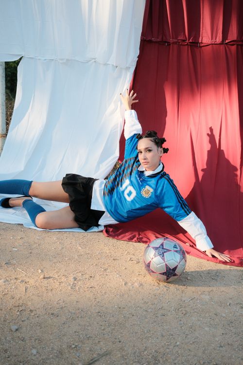 Free A young woman in a soccer jersey poses on sandy ground, showcasing sports enthusiasm. Stock Photo