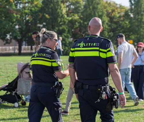 Free Two Dutch police officers at a public park, engaging with civilians during a daytime patrol. Stock Photo