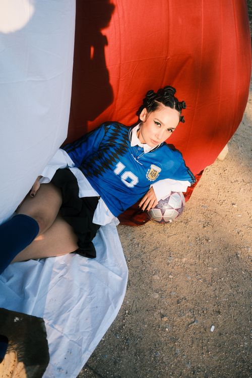 Free A young adult in a soccer jersey posing with a ball on a sandy outdoor setting. Stock Photo