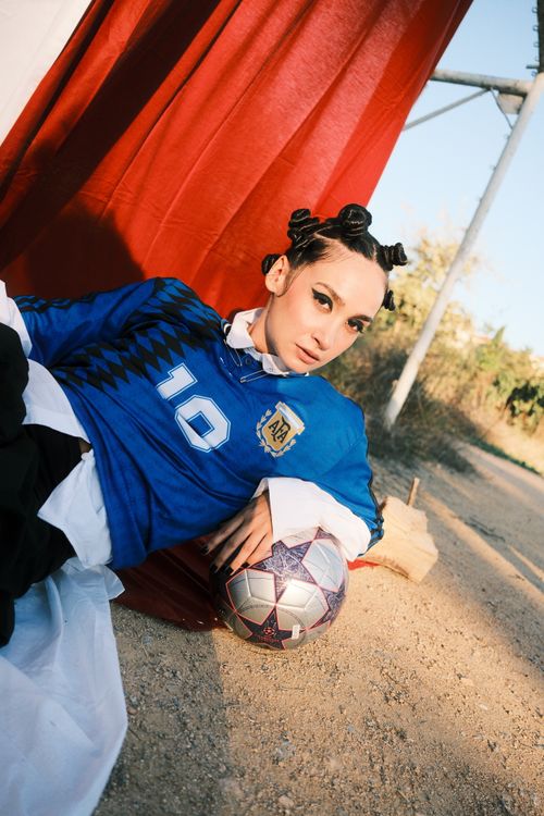 Free A young woman in a blue soccer jersey poses outdoors with a soccer ball. Stock Photo