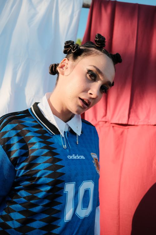 Free Woman posing in a vintage soccer jersey with bold background colors under sunlight. Stock Photo