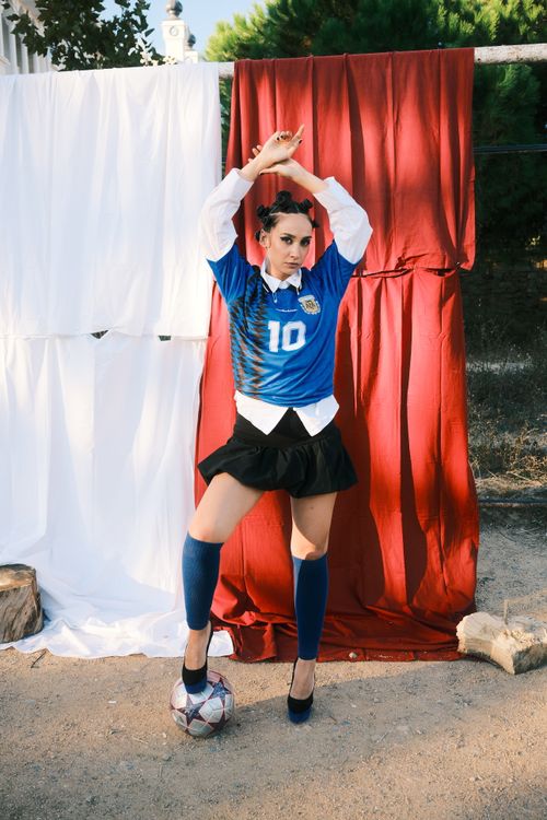 Free Confident woman in a blue soccer jersey poses outdoors, standing on a football. Stock Photo
