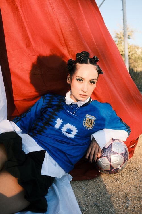 Free Woman poses outdoors in a soccer jersey holding a ball, conveying sporty style. Stock Photo