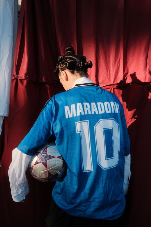 Free A young person in a Maradona jersey holding a soccer ball by a red curtain. Stock Photo