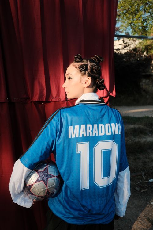 Free A young woman holding a soccer ball wearing a vintage Maradona jersey outdoors. Stock Photo