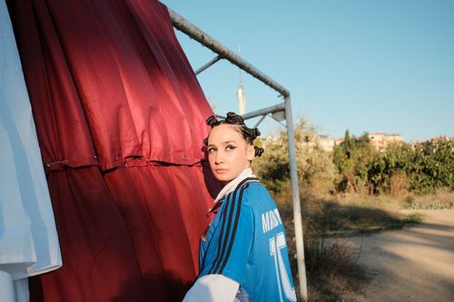 Free Woman with braided hair in a blue sports jersey stands by curtains outdoors on a sunny day. Stock Photo