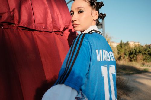 Free Woman in a retro soccer jersey stands outdoors, blending style and nostalgia. Stock Photo