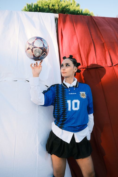 Free Woman in blue jersey balancing a soccer ball against a colorful backdrop outdoors. Stock Photo