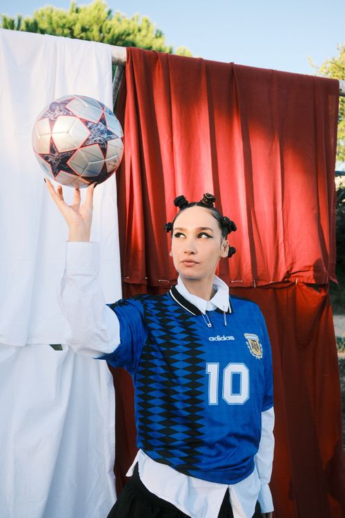 Free A trendy soccer fan skillfully holds a ball, dressed in a blue soccer jersey, outdoors. Stock Photo