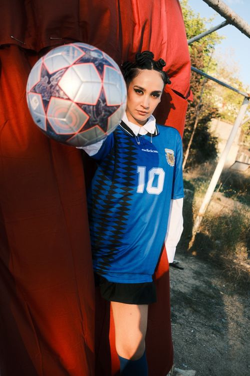 Free Confident female soccer player in blue jersey posing with ball outdoors, showcasing sportsmanship. Stock Photo