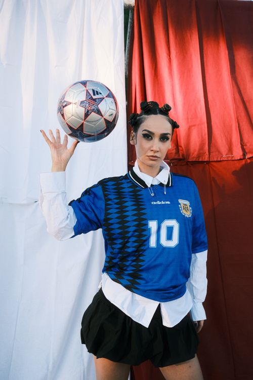 Free A fashionable soccer fan poses with a football against a vibrant fabric backdrop. Stock Photo
