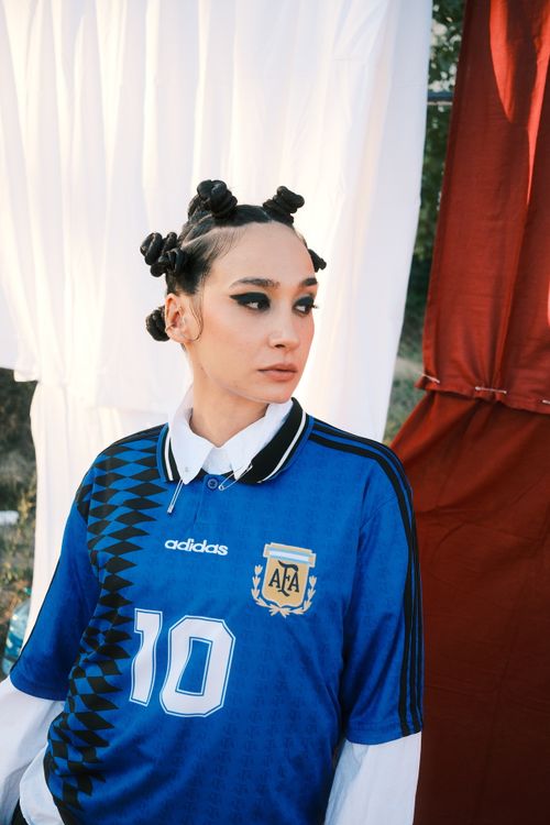 Free Stylish woman in blue soccer jersey with unique hairstyle against fabric backdrop. Stock Photo
