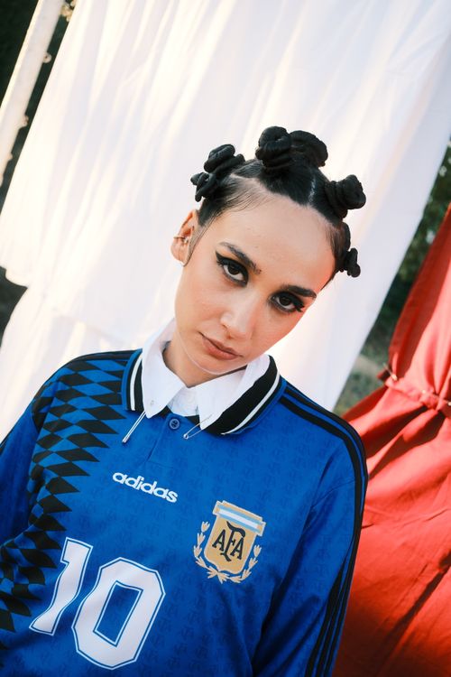 Free Fashionable young adult in Argentina soccer jersey poses outdoors with unique hairstyle. Stock Photo