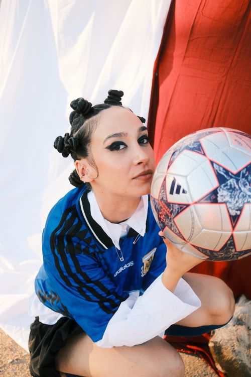 Free A stylish young woman in a sports jersey holding a soccer ball outdoors. Stock Photo