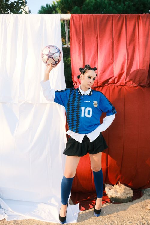 Free Confident woman in soccer jersey holding ball with colorful backdrop, showcasing athletic style. Stock Photo