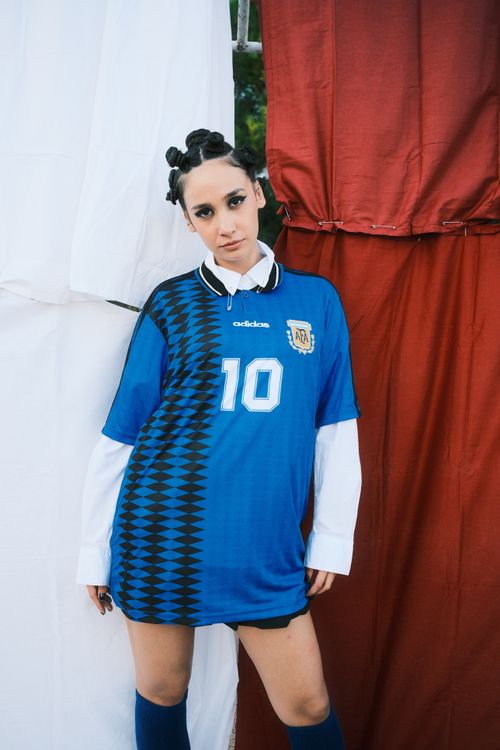 Free Young woman posing in a blue soccer jersey with a bold hairstyle and confident expression. Stock Photo