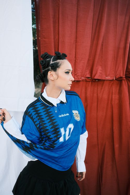 Free Woman wearing a retro soccer jersey with artistic hairstyle in a modern setting. Stock Photo