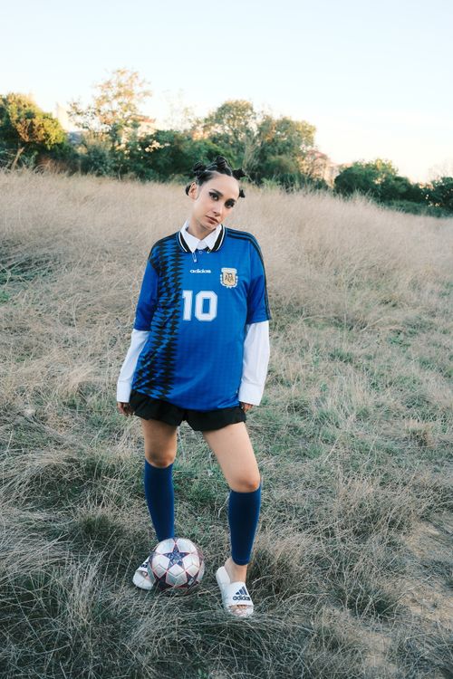 Free Teen soccer player in blue jersey with ball, outdoor setting. Stock Photo