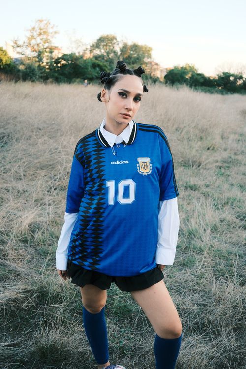 Free Young woman in a blue soccer jersey standing in a field, showcasing sporty style. Stock Photo