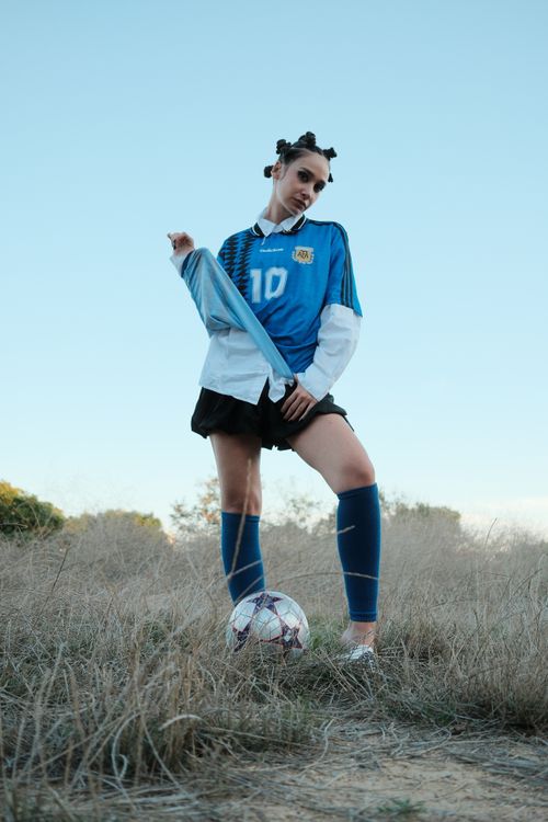 Free Confident young woman posing outdoors in a soccer jersey with football on a grassy field. Stock Photo