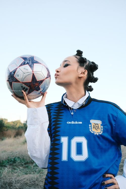 Free Confident woman kisses a soccer ball while wearing a team jersey, outdoors. Stock Photo