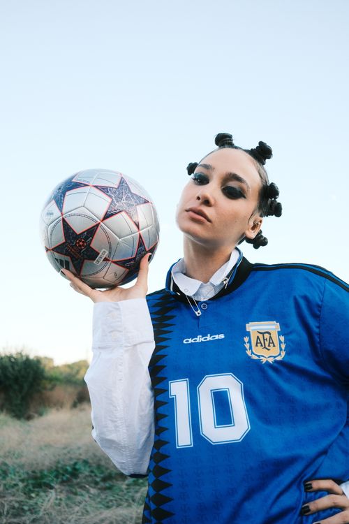 Free Portrait of a woman holding a soccer ball wearing a blue football jersey, captured outdoors. Stock Photo