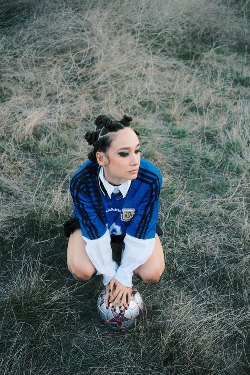 Free A young woman crouches outdoors in a soccer jersey, holding a ball. Stock Photo