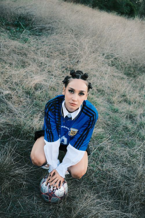 Free Portrait of a young woman in a football jersey outdoors, holding a soccer ball. Stock Photo