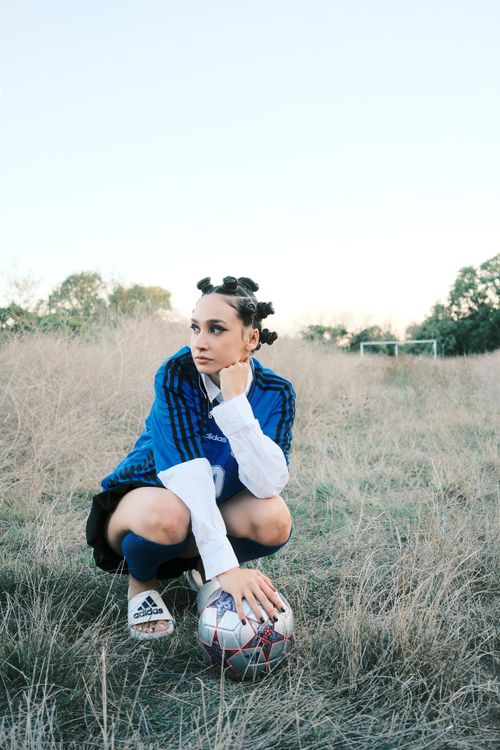 Free A young woman soccer player crouching on a grassy field with a ball. Stock Photo
