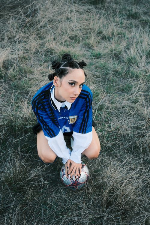 Free Young woman in blue soccer jersey kneeling on grass with soccer ball, outdoors. Stock Photo