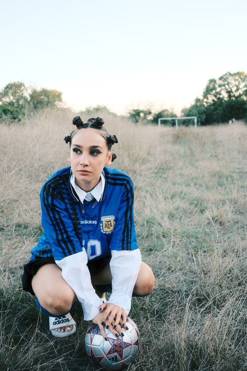 Free Young woman in soccer jersey crouching with a ball on a grassy field, ready to play. Stock Photo