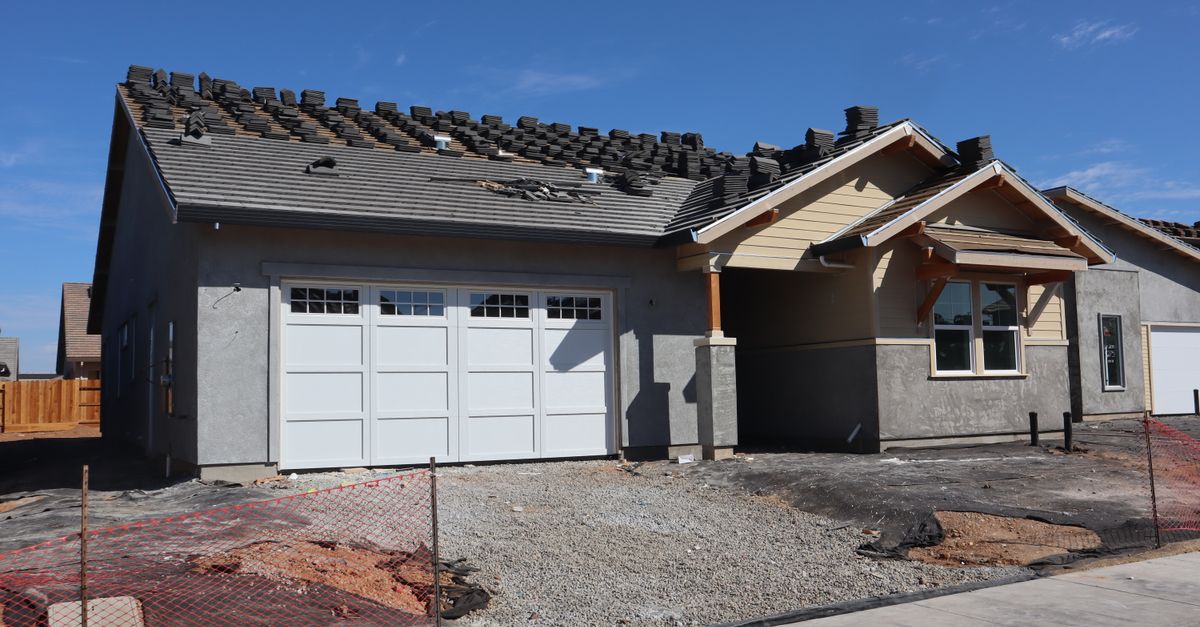 Modern suburban home under construction showcasing roof tiles being installed against a clear sky.