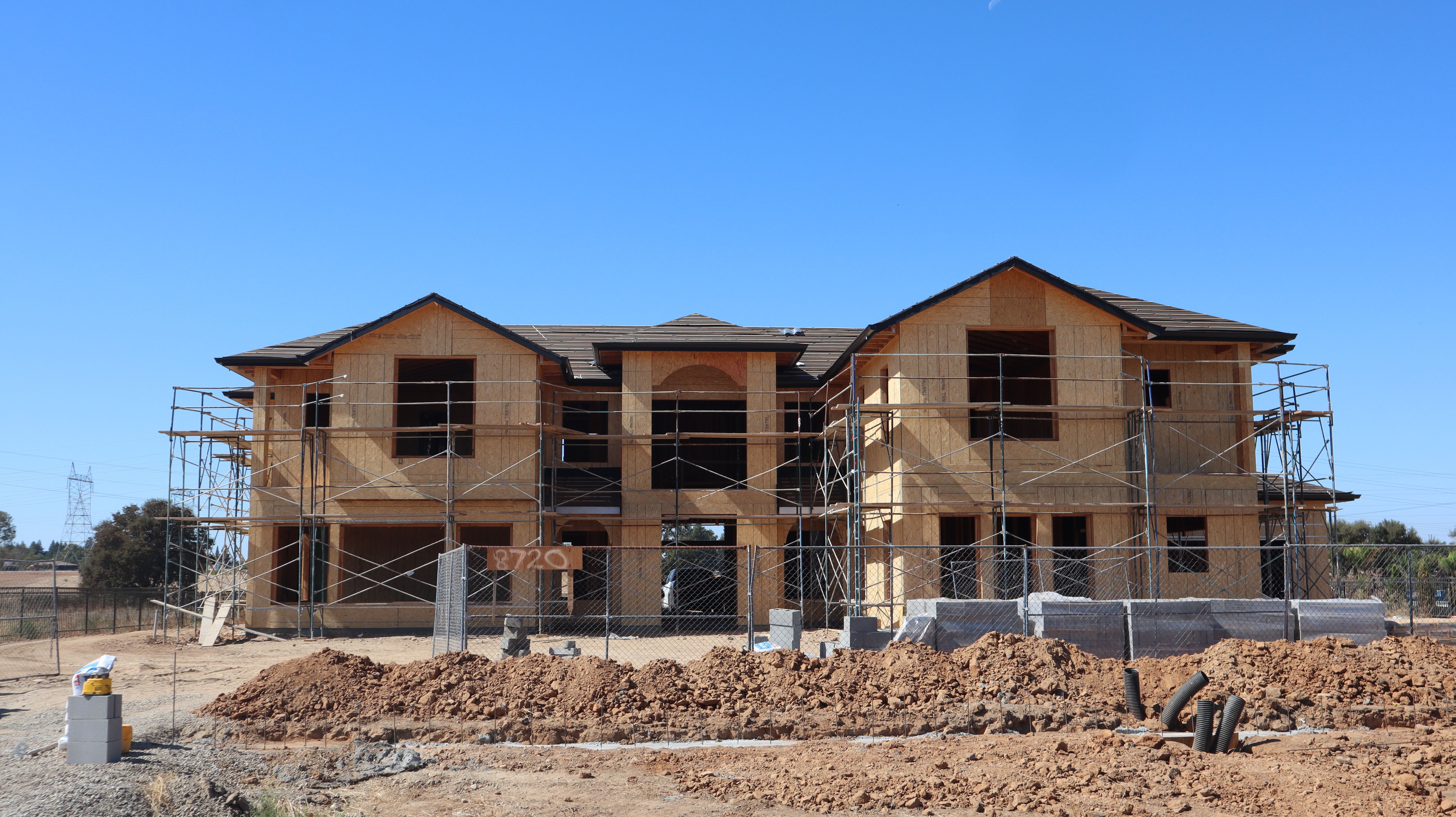 Newly constructed two-story house with scaffolding under a clear blue sky.