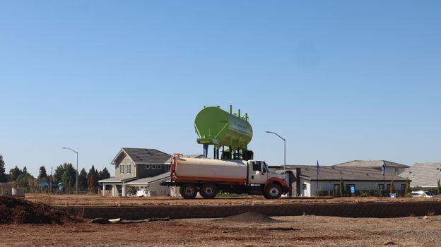 A water tanker truck at a residential construction site under a clear blue sky. - Fotografer Sidoarjo