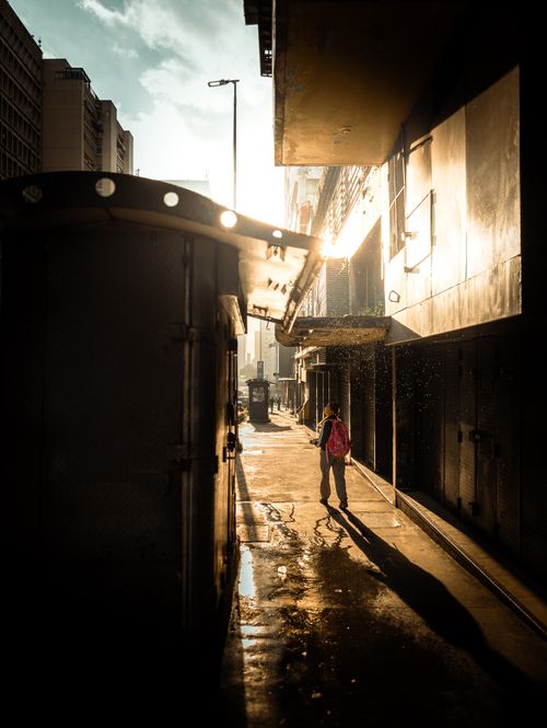Free A lone figure walks down a sunlit alley in Caracas during golden hour, casting long shadows. Stock Photo