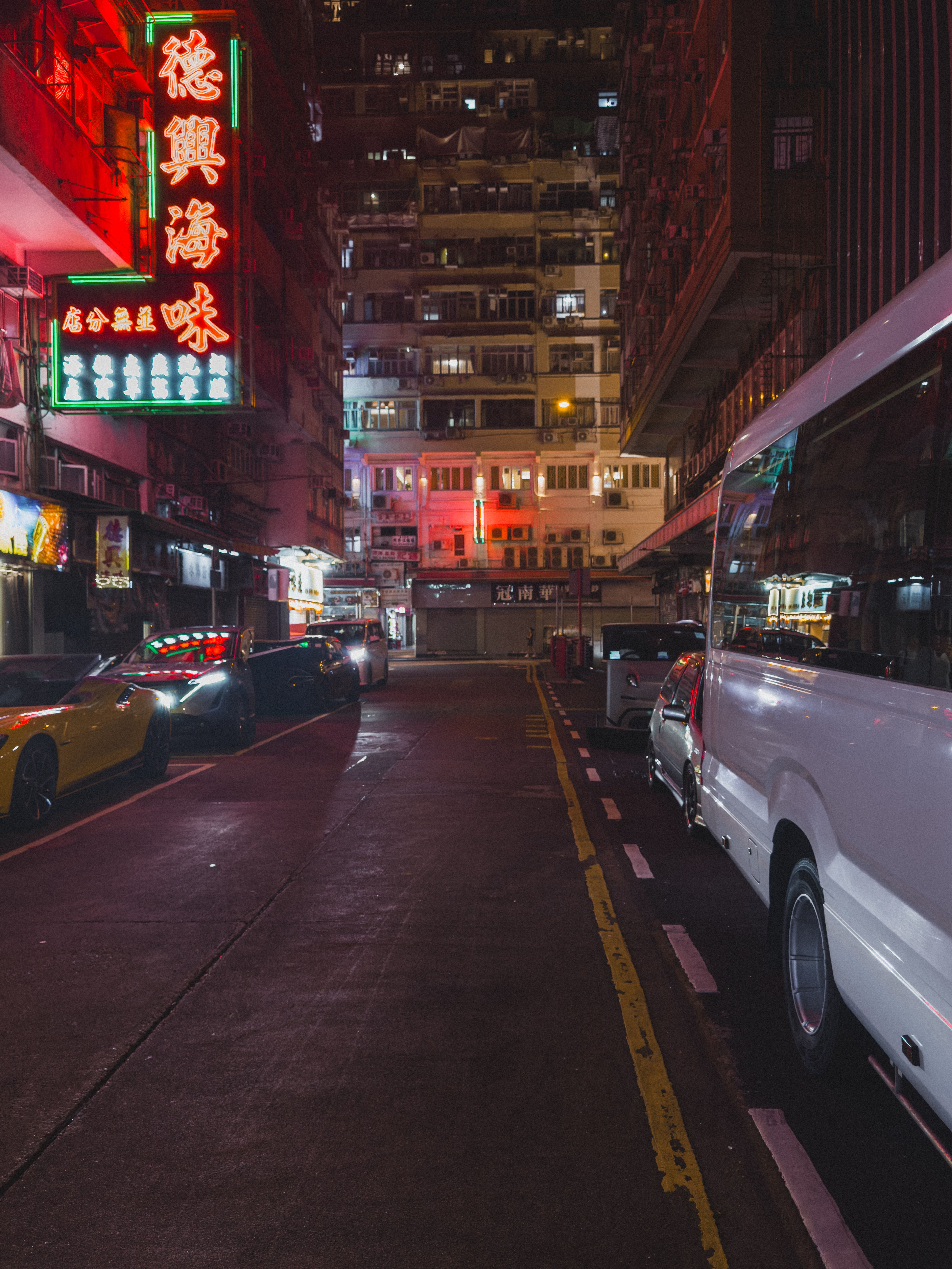 Moody street view of Hong Kong at night with neon lights and parked cars.