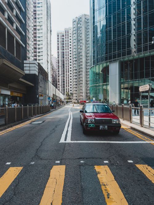 Free A street in Hong Kong featuring a red taxi amidst skyscrapers, showcasing urban architecture. Stock Photo