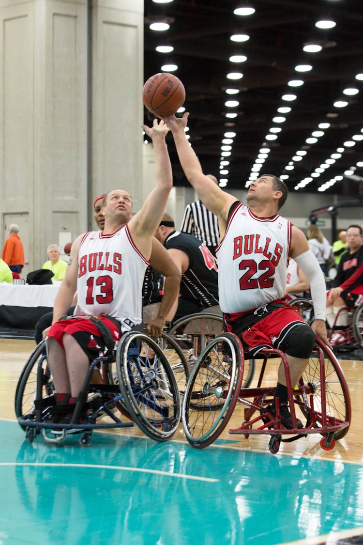 Two Men In White And Red Jersey Shirts Playing Basketball On Wheelchairs