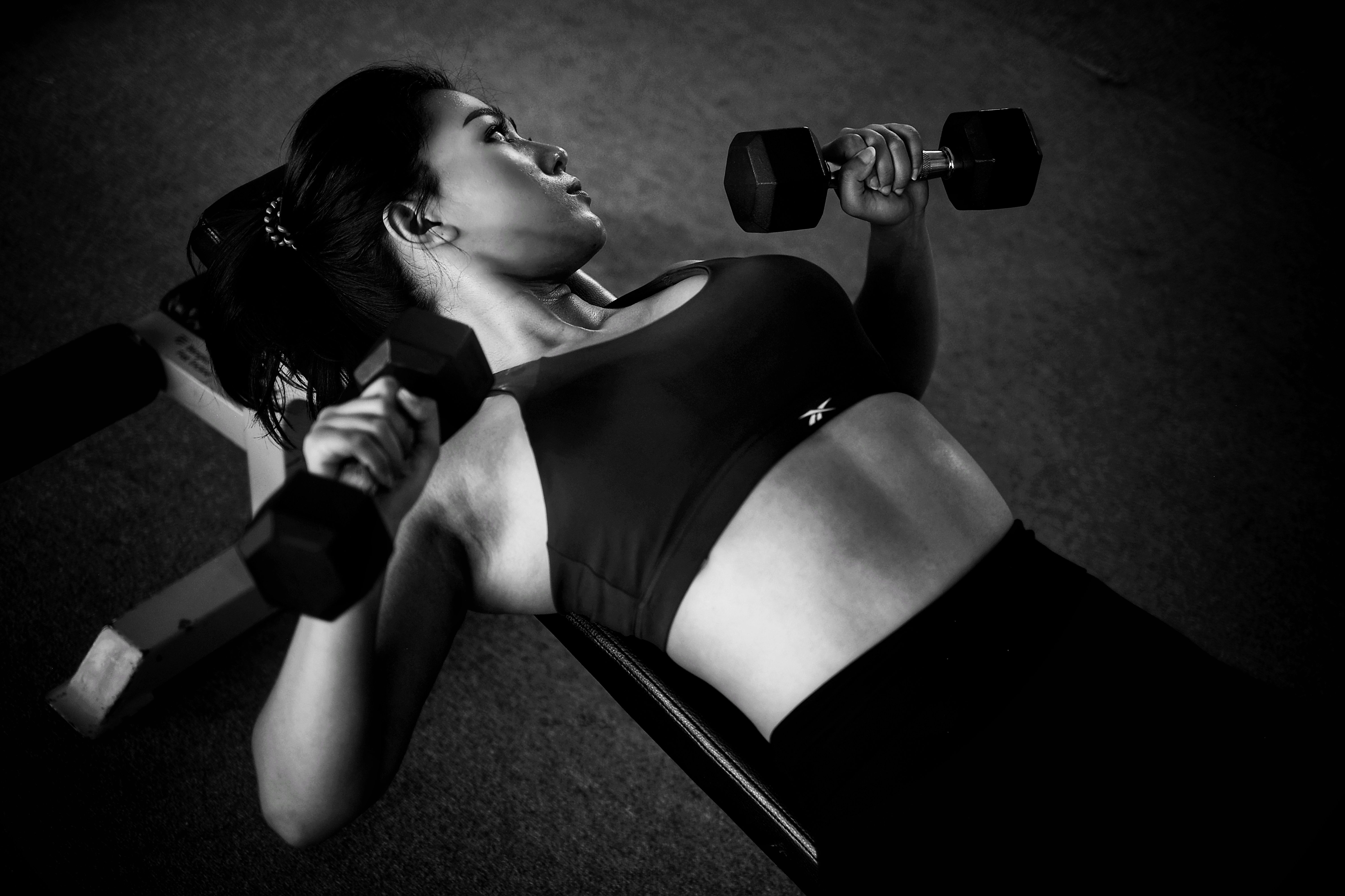 Woman doing bench weight training with dumbbells in a gym