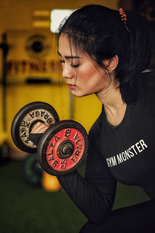 Free Focused young woman lifting dumbbells in a gym environment, emphasizing strength and fitness. Stock Photo