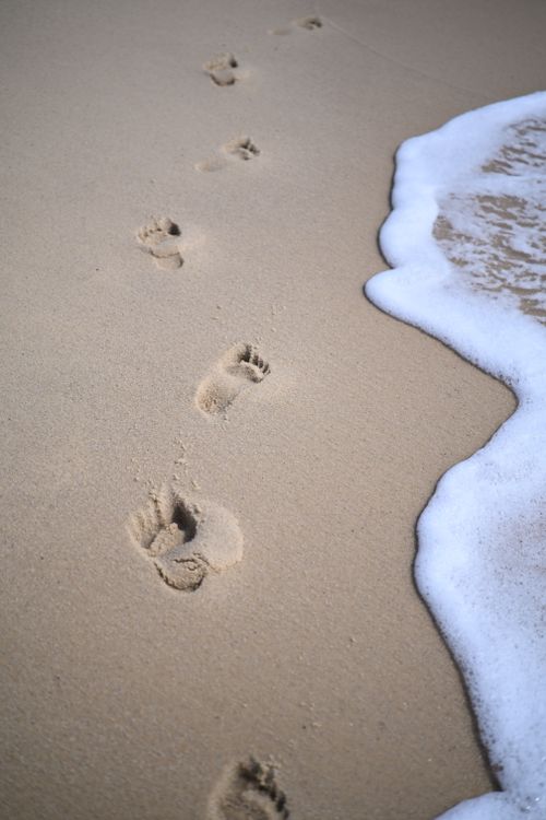 Free Footprints in sand near ocean waves capture serene beach moment. Stock Photo