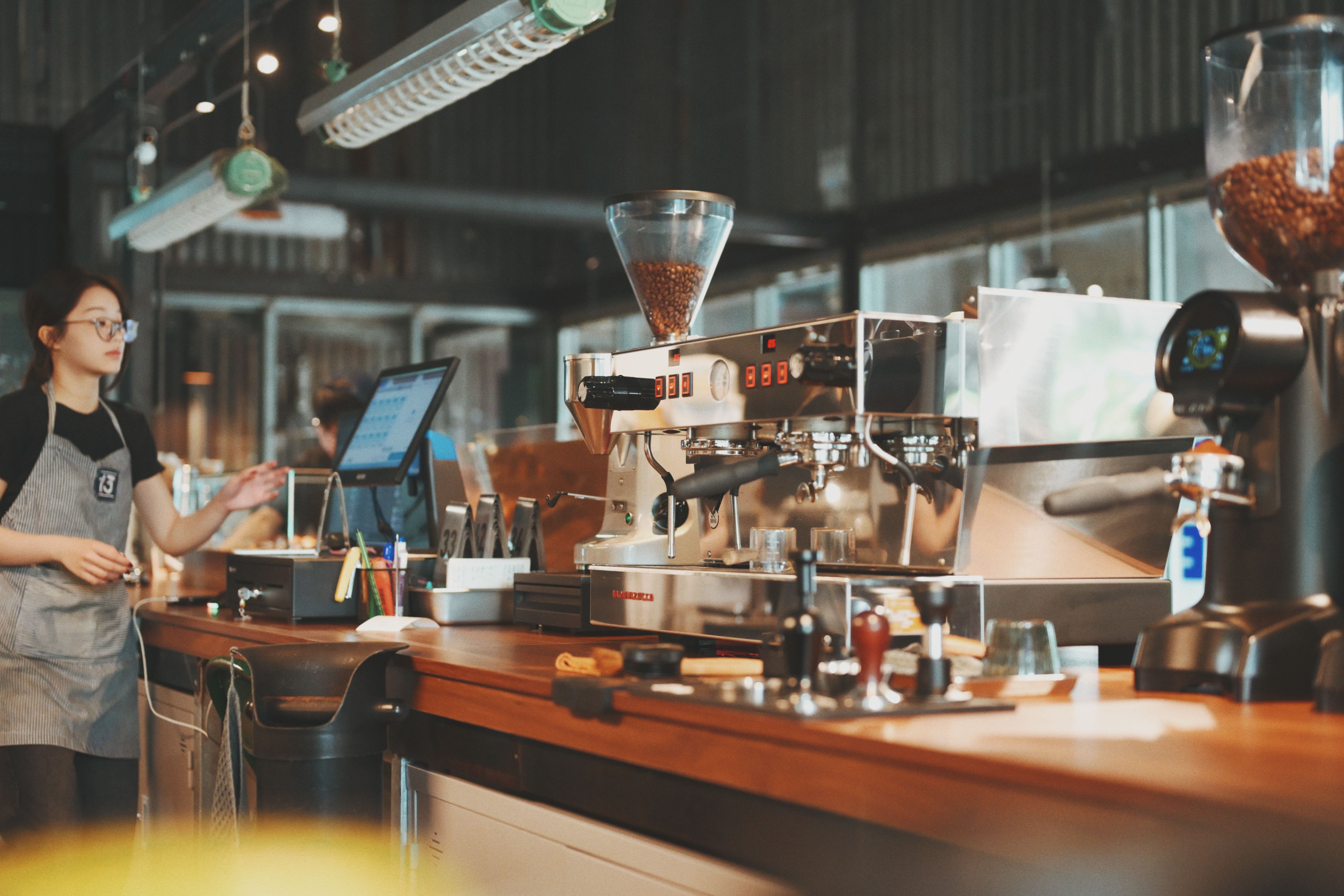 Barista at coffee shop counter using espresso machine for fresh brew coffee.