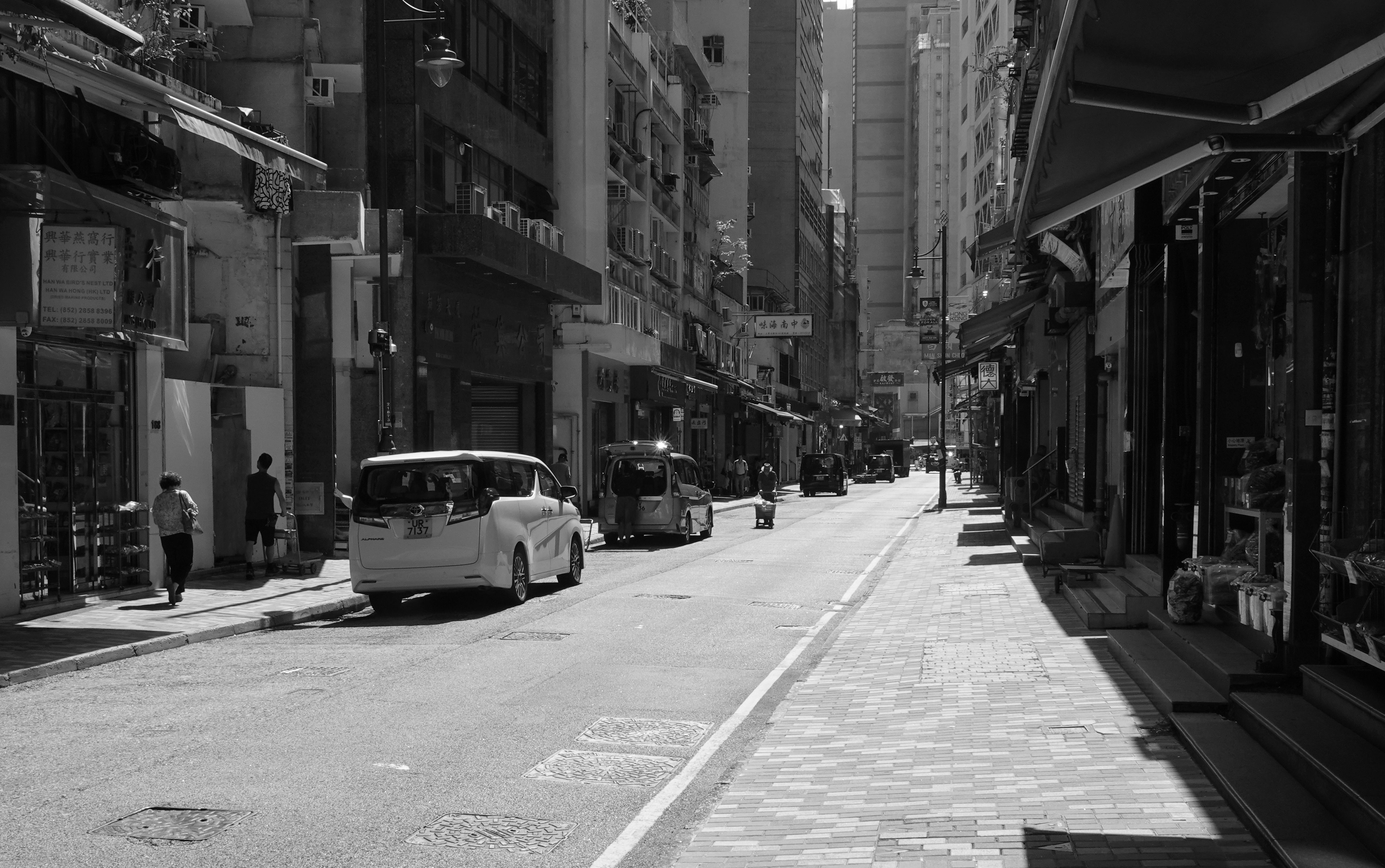 Black and white photo capturing a traditional street in Sheung Wan, highlighting Hong Kong's urban life.