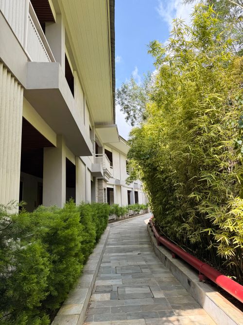 Free Contemporary building facade alongside a lush, green-lined walkway under a clear sky. Stock Photo